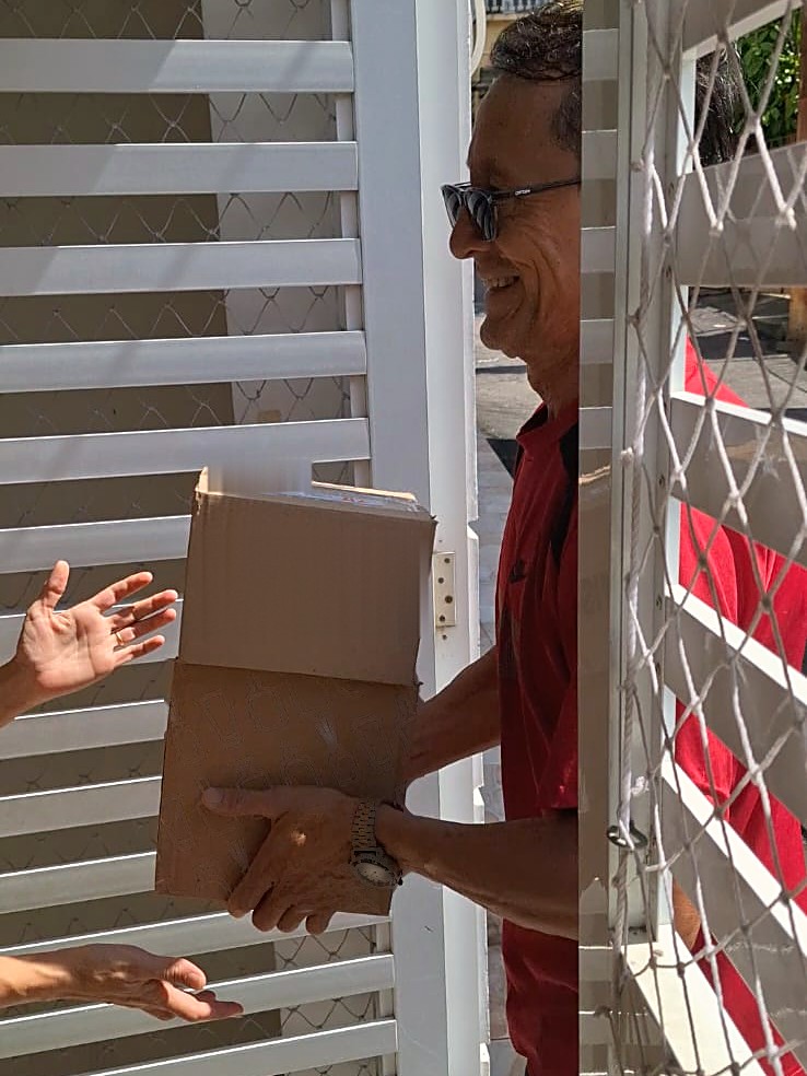 Entregador da É Coisa Bio sorrindo ao entregar a caixa nas mãos de uma cliente, no portão de casa
